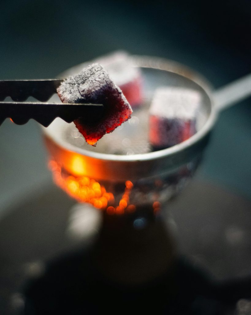 Close-up of glowing hookah charcoal with tongs in dim lighting, ideal for nightlife concepts.